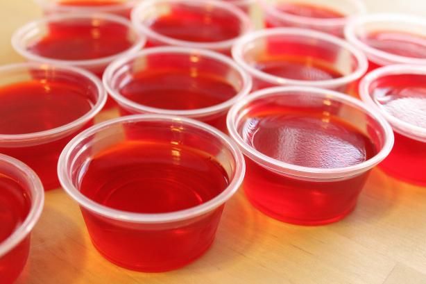 several cups filled with red liquid sitting on top of a wooden table next to each other