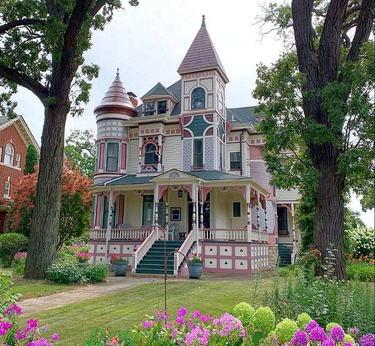 a pink and white victorian style house surrounded by flowers