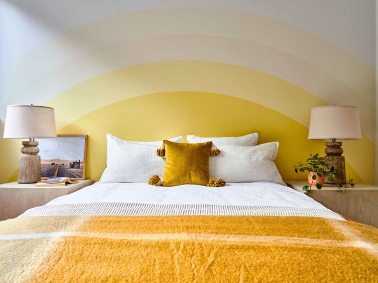 a yellow and white bedroom with two lamps on either side of the bed, one lamp is turned on