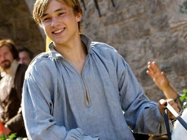 a young man smiles as he walks his horse with two other men behind him in the background