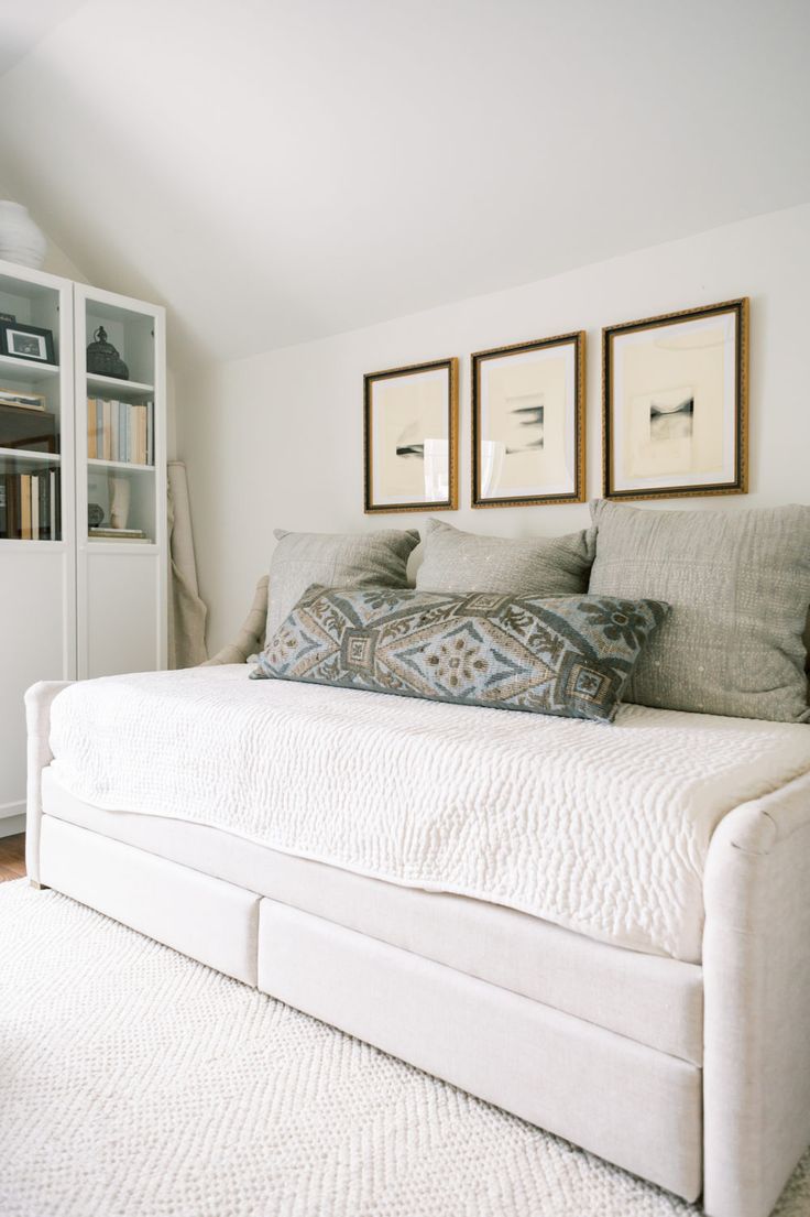 a white daybed with pillows and pictures on the wall