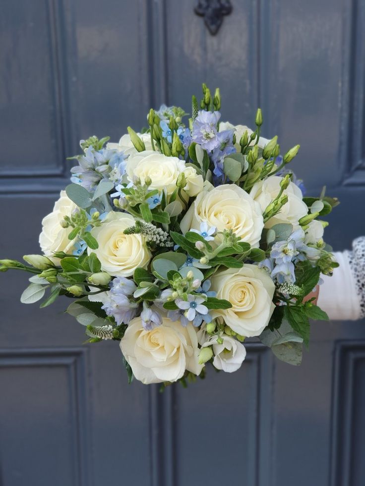 a bouquet of white roses and blue flowers in front of a door with green leaves