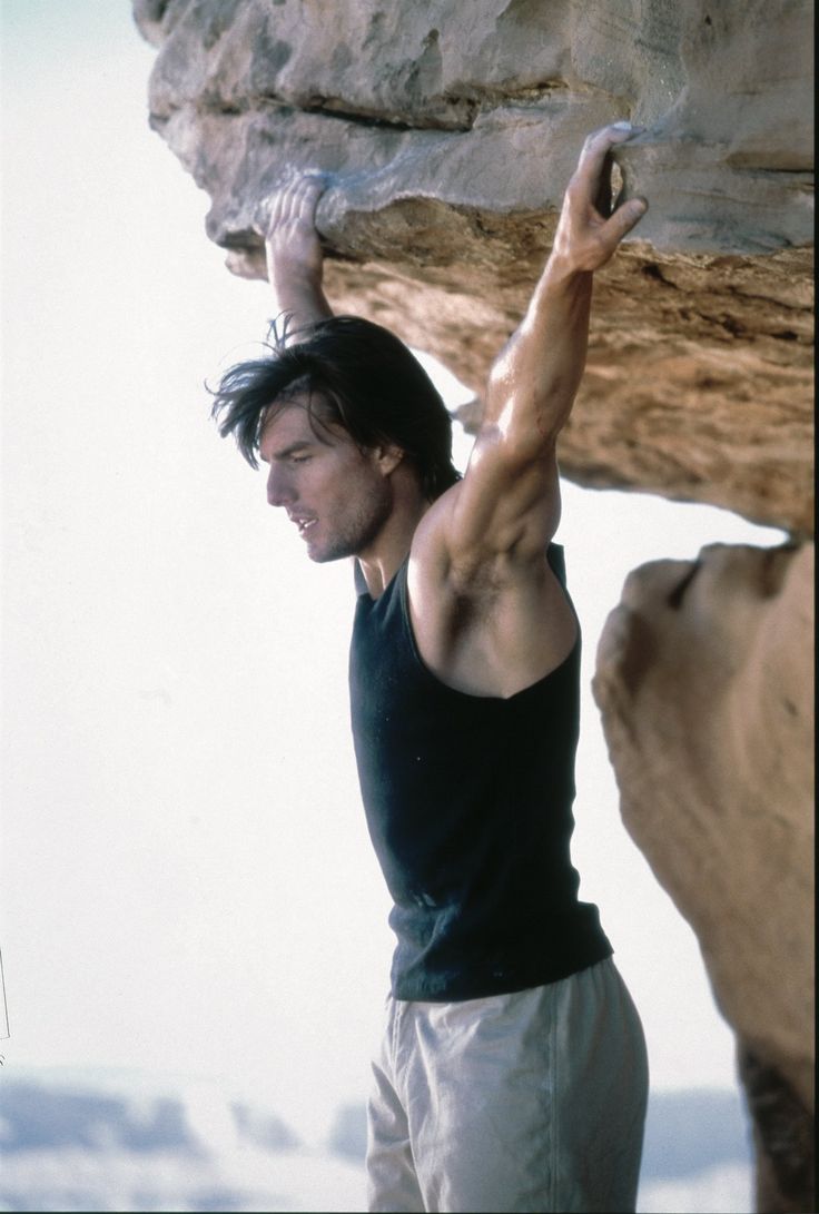 a man climbing up the side of a cliff with his hands in the air while holding onto a rock