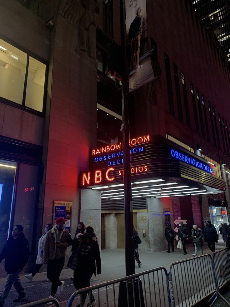 people walking on the sidewalk in front of a building with neon signs at night time