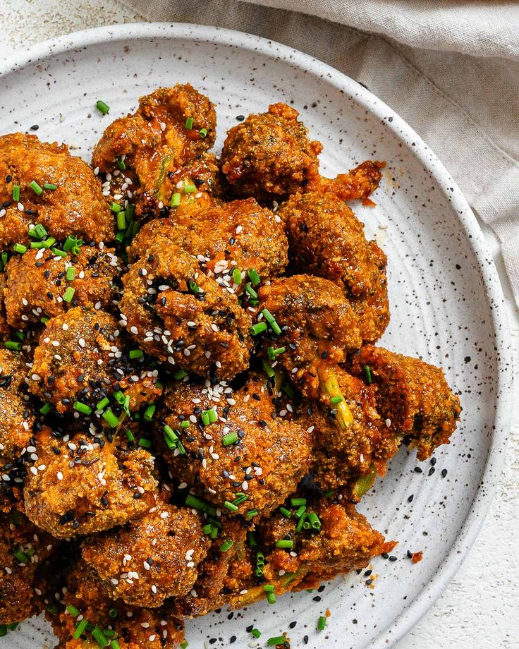 a white plate topped with meatballs covered in sesame seeds and seasoning sprinkled with green onions