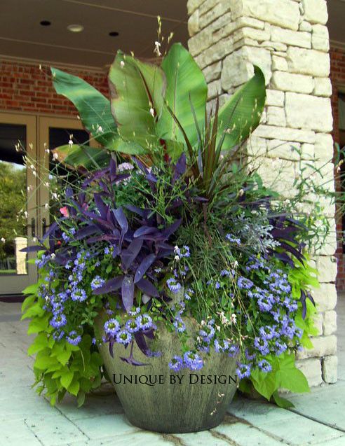 a planter filled with lots of purple flowers and greenery next to a brick building