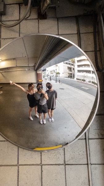 three people standing in front of a mirror on the ground and one person pointing at something