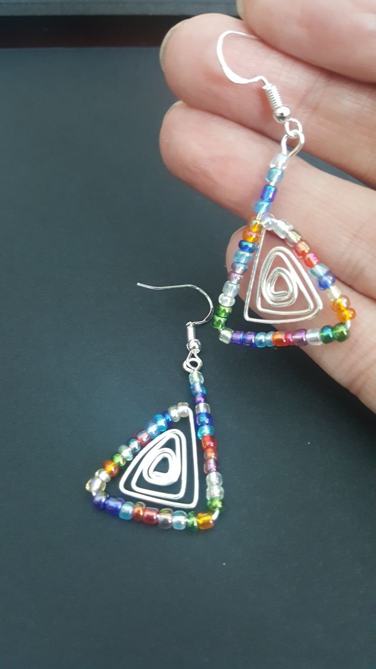 a pair of colorful beaded triangle shaped earrings on a person's palm hand