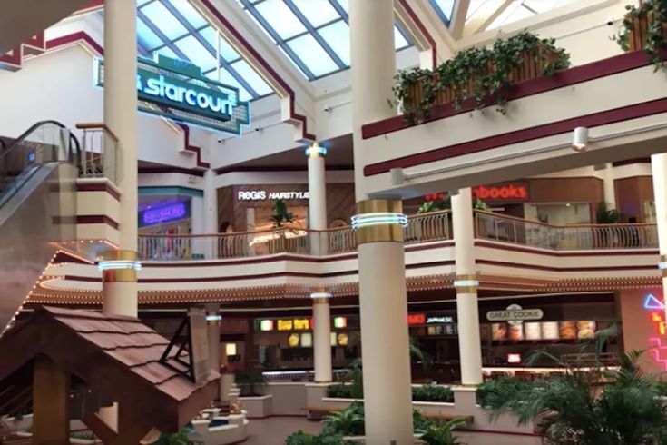 the inside of a shopping mall filled with lots of plants and people walking through it