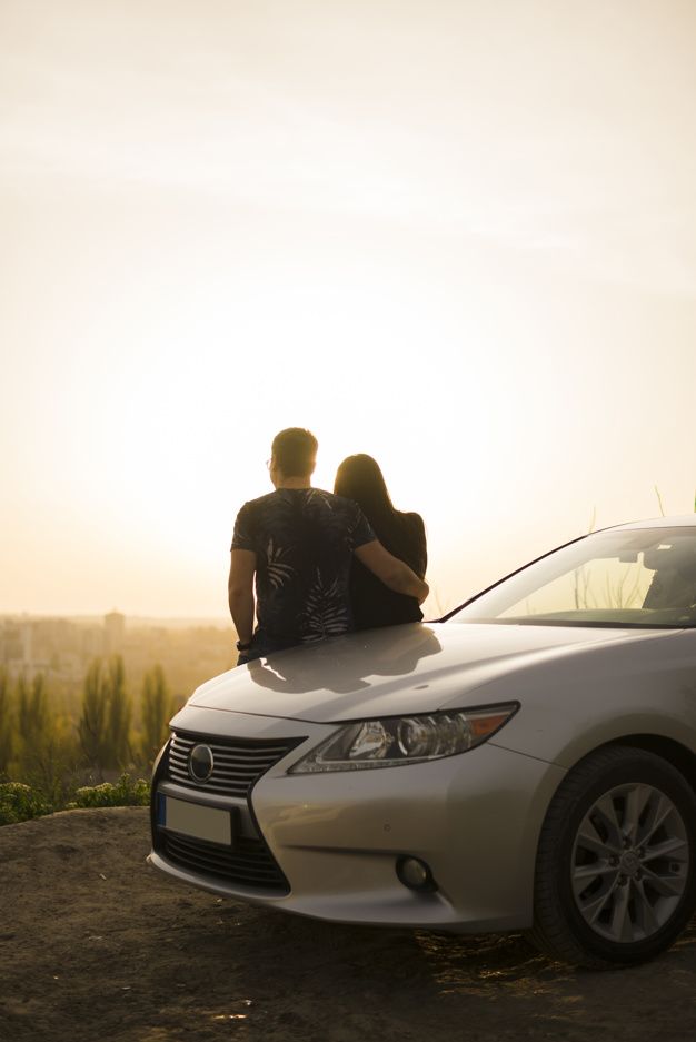 two people are sitting on the hood of a car in front of a scenic view