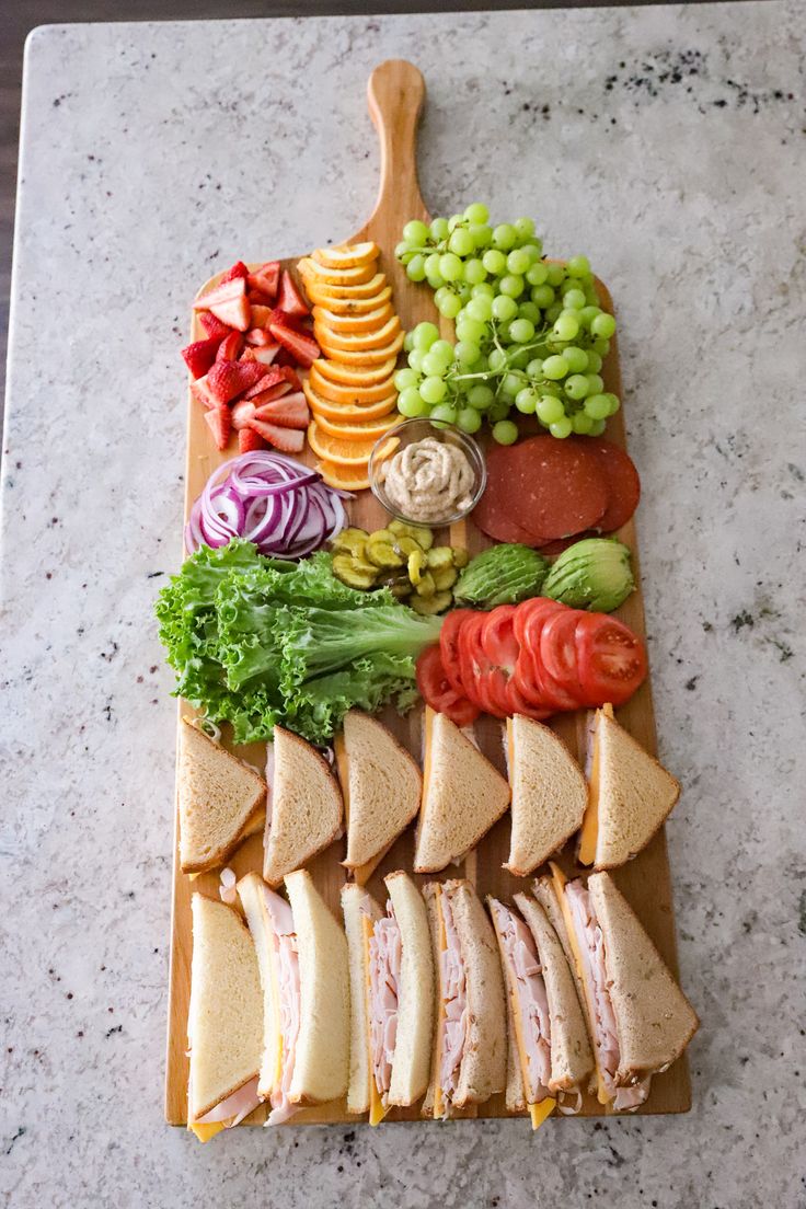 a wooden cutting board topped with cut up sandwiches and veggies on top of it