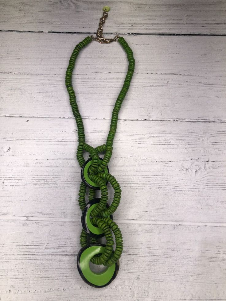 a green and black necklace is hanging on a white wall