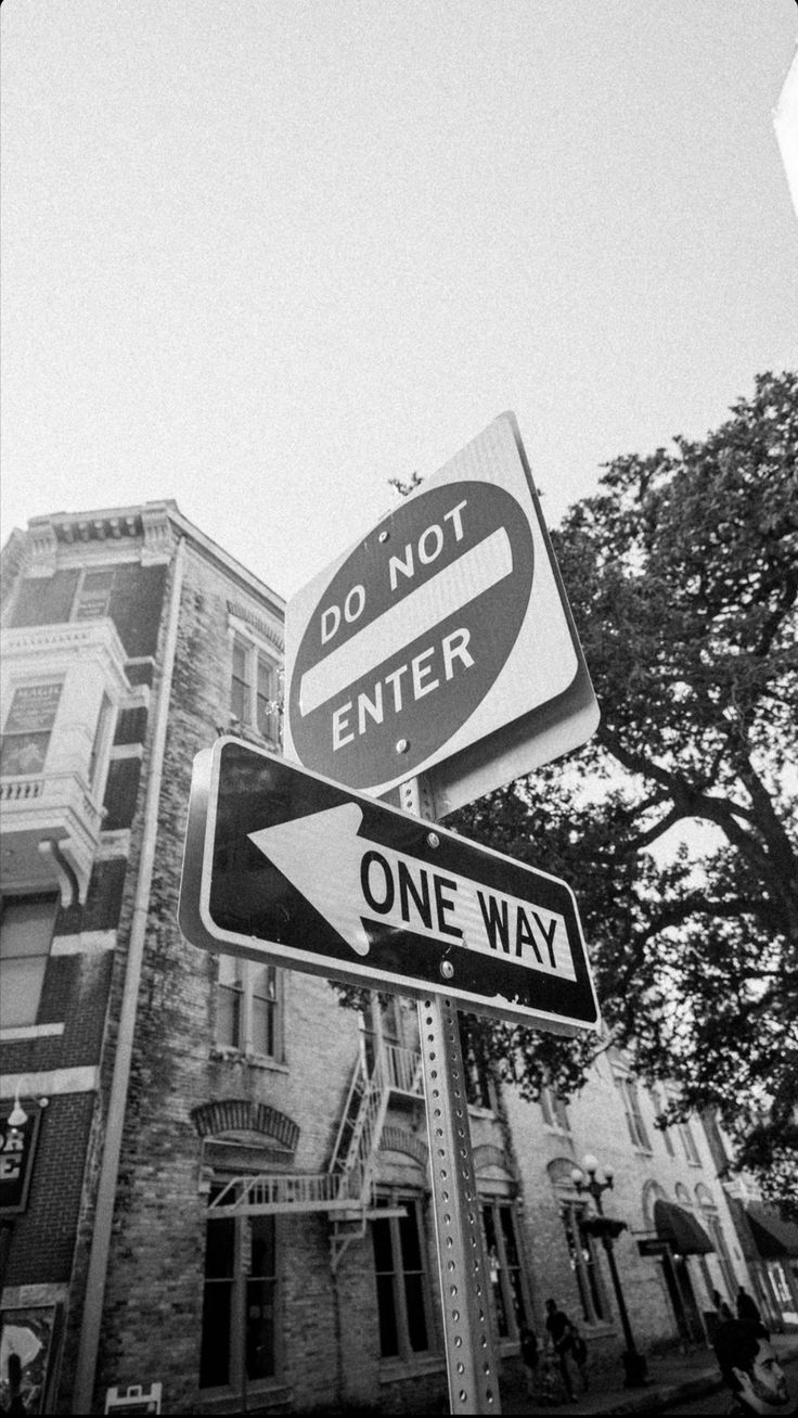 black and white photograph of two street signs in front of an old building with the words do not enter on it