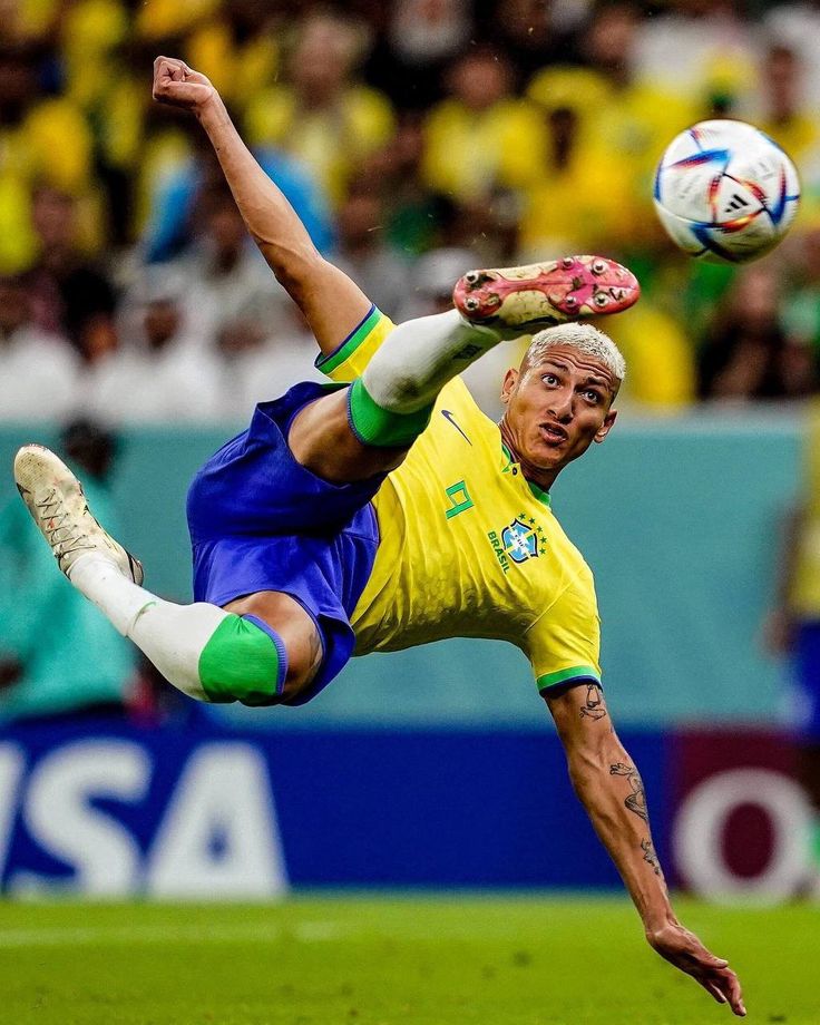 a man kicking a soccer ball on top of a field with other people in the background