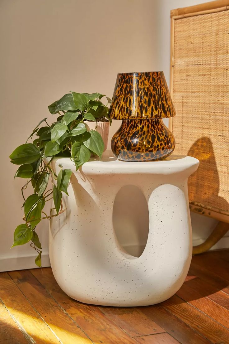 a plant sits on top of a white vase with a leopard print lamp shade next to it