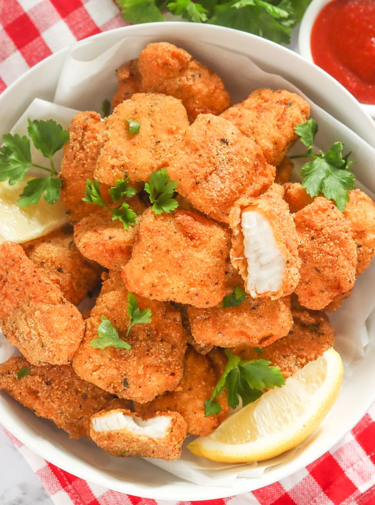 a white bowl filled with fried chicken nuggies next to a red and white checkered tablecloth