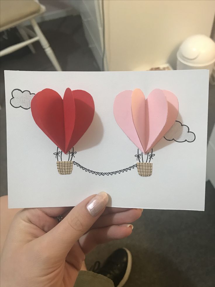 someone is holding up two heart shaped balloons on a string attached to a white card