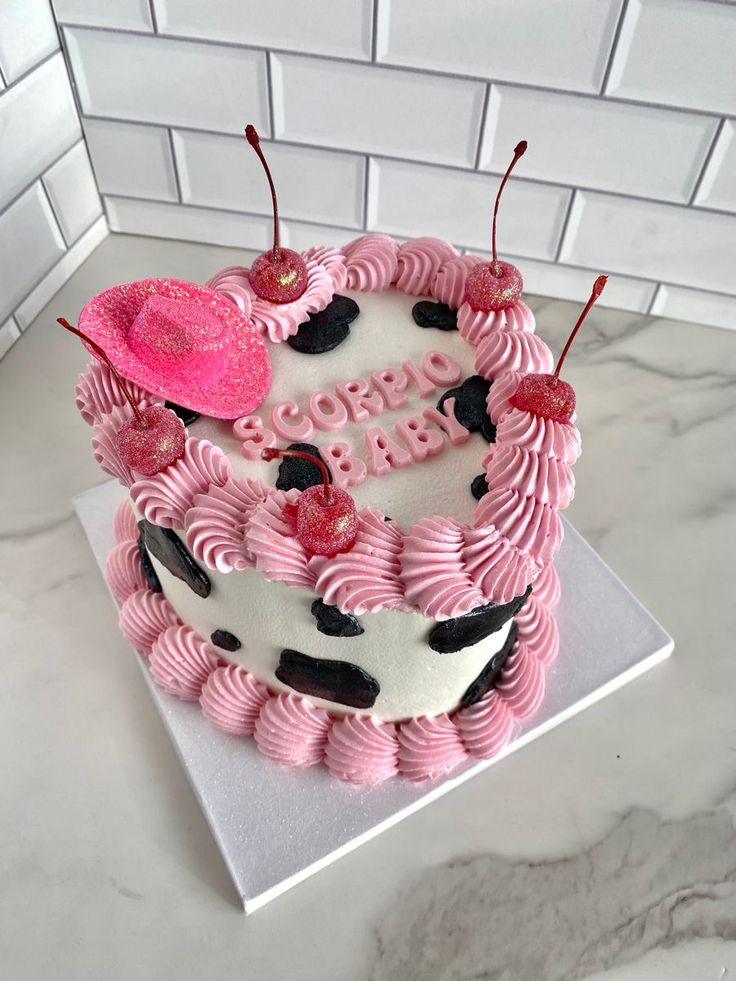 a birthday cake with pink frosting and cow print decorations on the top, sitting on a marble countertop