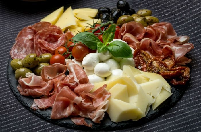 a black plate topped with lots of different types of cheese and meats next to olives