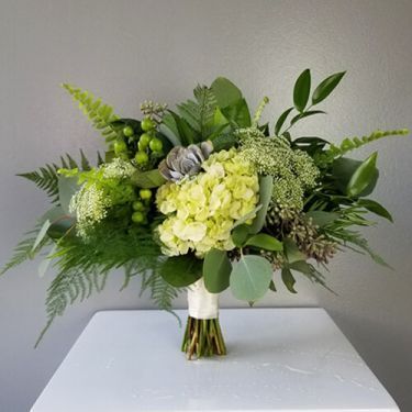 a vase filled with green flowers and greenery on top of a white countertop