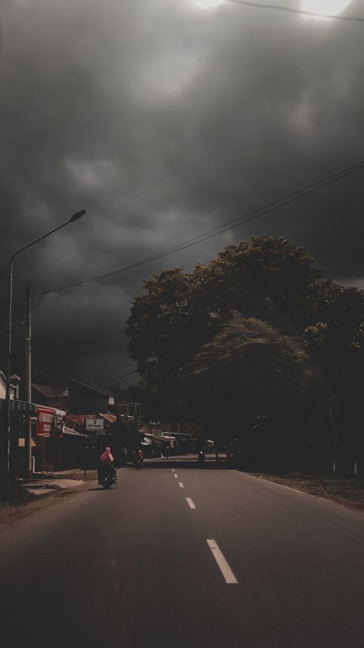 a person riding a motorcycle down a street under dark clouds