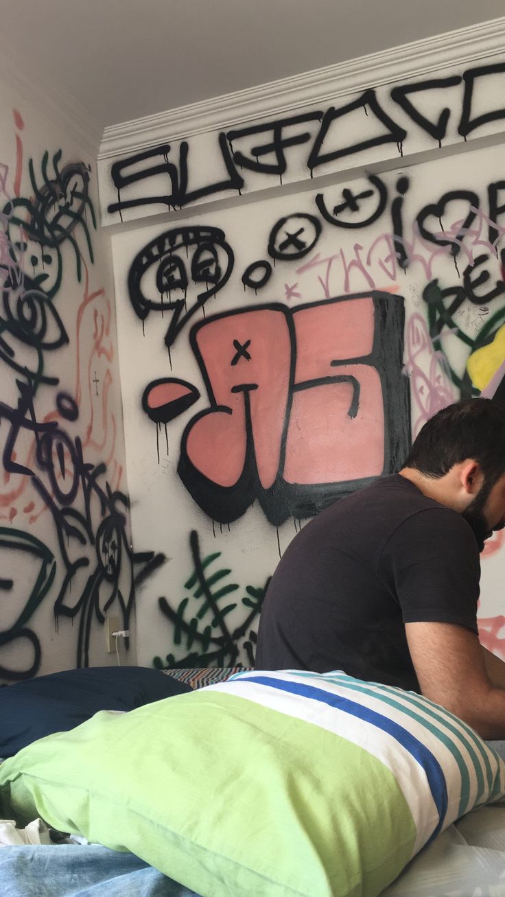 a man sitting on top of a bed next to a wall covered in grafitti