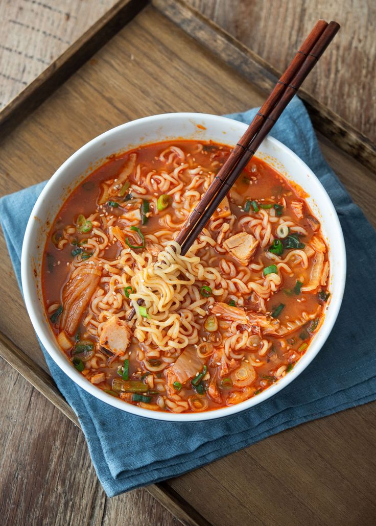 a bowl of noodles and meat soup with chopsticks on a wooden table top