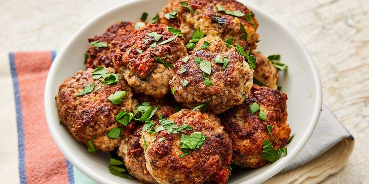 a white bowl filled with meatballs and garnished with parsley on top