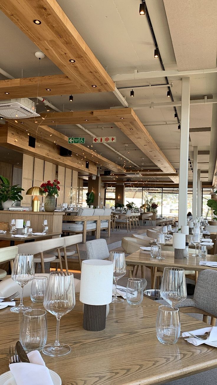 an empty restaurant with wooden tables and white linens on the table, along with wine glasses