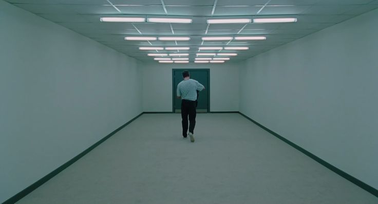 a man is walking down the hallway in an empty building with bright lights on the ceiling