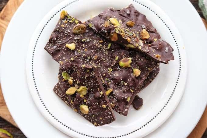 a white plate topped with pieces of chocolate covered in pistachios and nuts