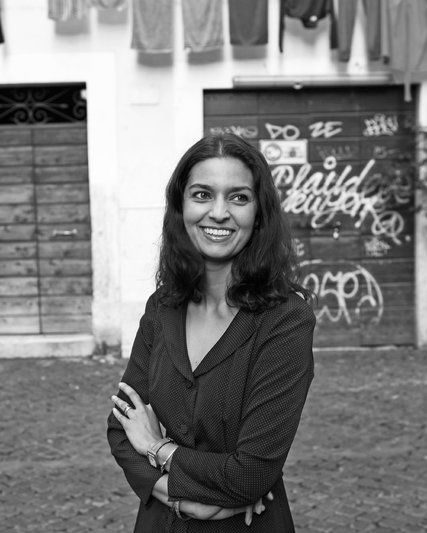 a black and white photo of a woman standing with her arms crossed in front of a building