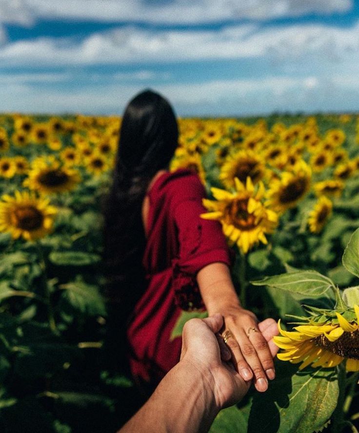 a woman in a red dress is walking through a sunflower field with her hand on the flower