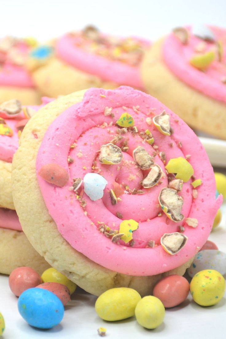 some cookies with pink frosting and sprinkles next to candy candies