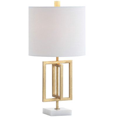 a table lamp with a white shade on the base and a gold frame around it