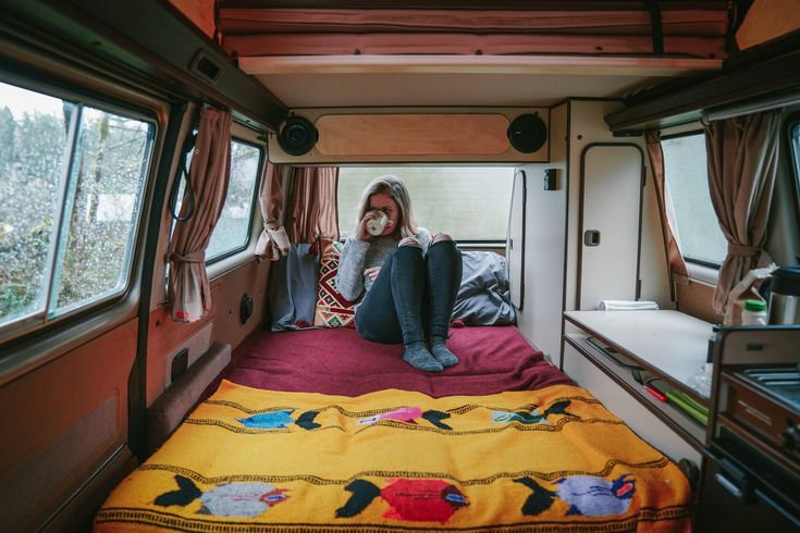 a woman is sitting on the bed in her camper van looking out the window