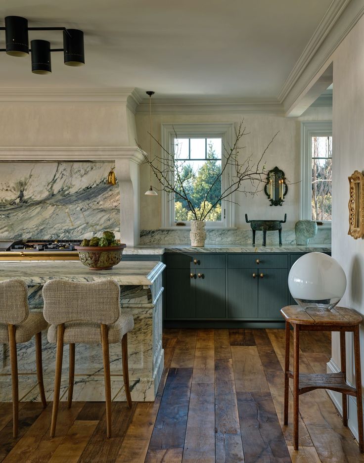 a kitchen with wooden floors and marble counter tops, along with two chairs that are facing an island