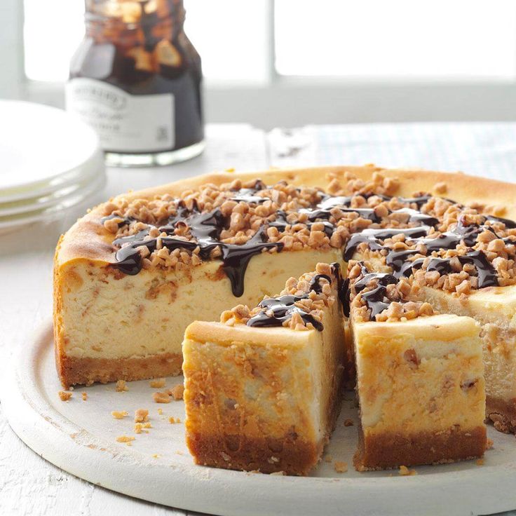 a cheesecake with chocolate toppings on a plate next to two plates and a bottle