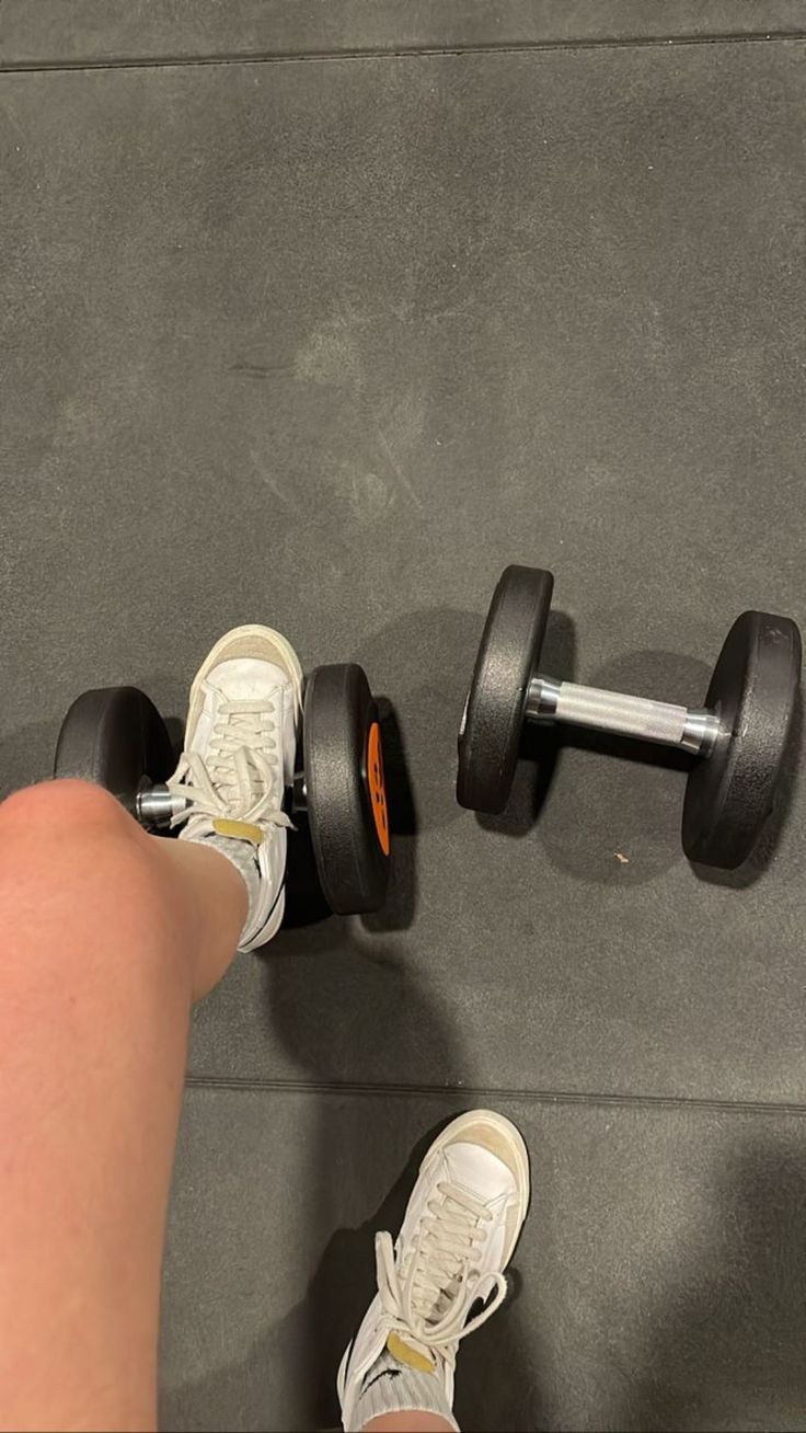 a person with their foot on a dumbble weight machine and one hand holding the barbell