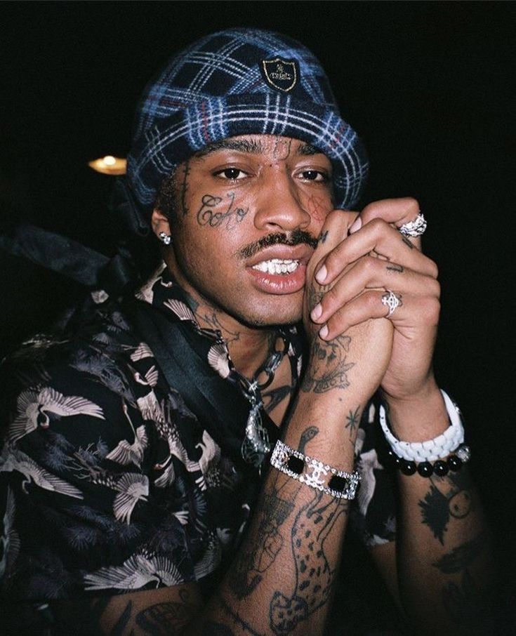 a young man with tattoos on his arm and wearing a blue plaid hat is posing for the camera