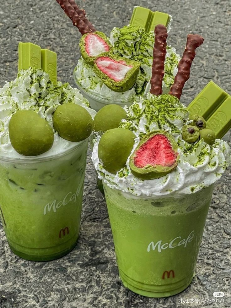 three green smoothies with fruit on top and chocolate sticks sticking out of the tops