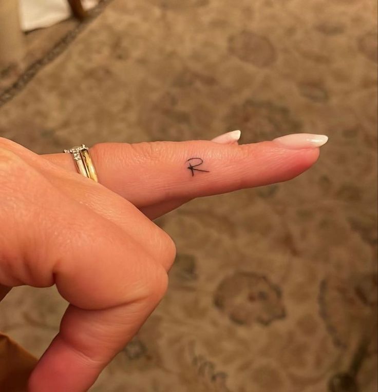 a woman's hand with a tiny ring on it and a small arrow tattoo on the middle finger