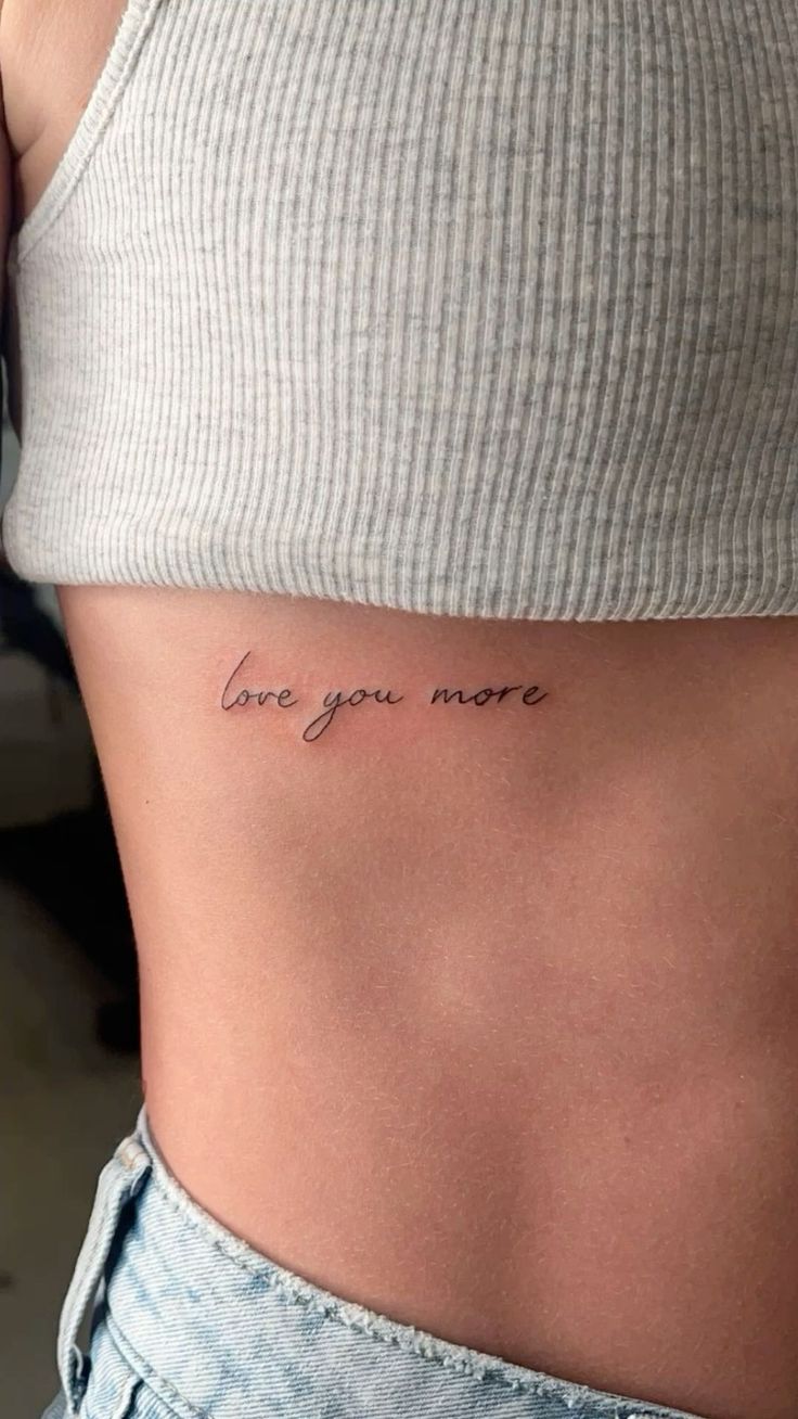 a woman's stomach with the words love you more tattooed on her lower back