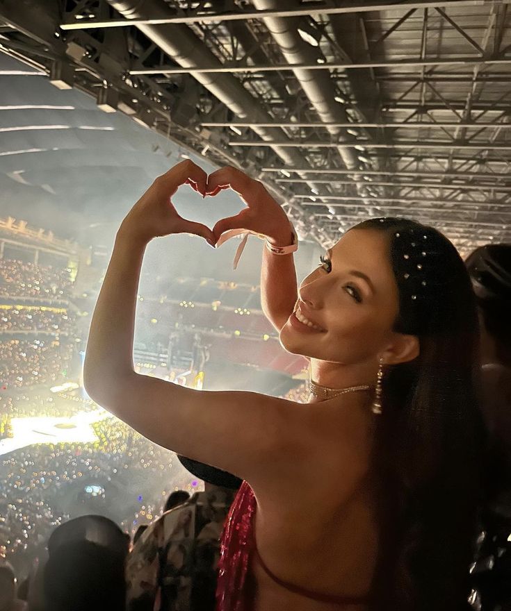 a woman in a red dress making a heart shape with her hands at a concert