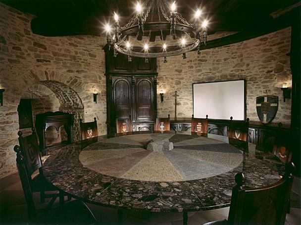 a circular table with chairs around it in front of a projector screen and fireplace