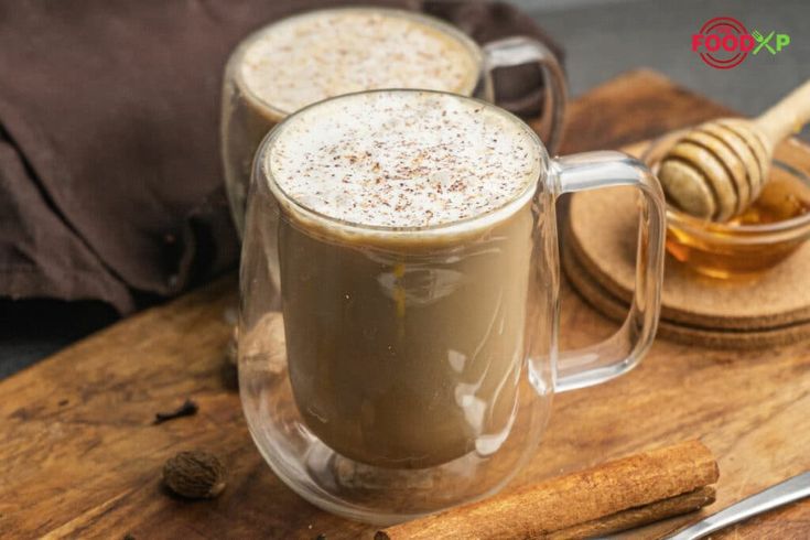 two mugs filled with liquid sitting on top of a wooden cutting board next to cinnamon sticks