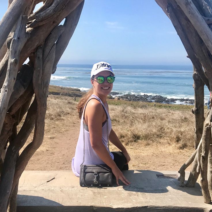 a woman sitting on the edge of a wooden structure near the ocean with her hands in her pockets