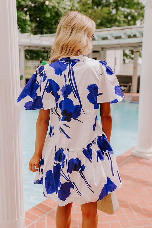 - Stay polished and pretty in this darling dress! Designed with a beautiful floral print and ruffle detailing, this piece is perfect for stylish days under the sun. - Fully lined material with a blue hued abstract floral print - A v-cut neckline with gathered detailing - Short loose sleeves - A relaxed silhouette that ends in a straight mini dress length hemline Blue Floral Sundress For Brunch, Blue Floral Print Mini Dress For Brunch, Blue Floral Print Mini Dress For Day Out, Blue Floral Short Sleeve Dress For Garden Party, Chic Blue Printed Floral Dress, Blue Floral Sundress For Day Out, Blue Floral Sundress For Garden Party, Blue Floral Print Short Sleeve Dress, Blue Floral Print Dress For Day Out