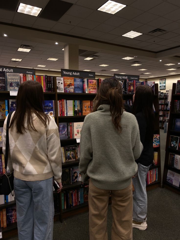 two women standing in front of a bookshelf with many books on the shelves