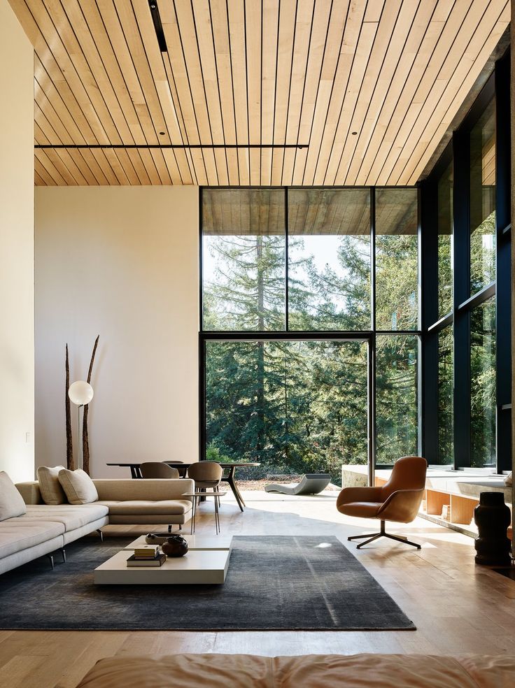 a modern living room with large windows and wood ceilinging, along with an area rug on the floor